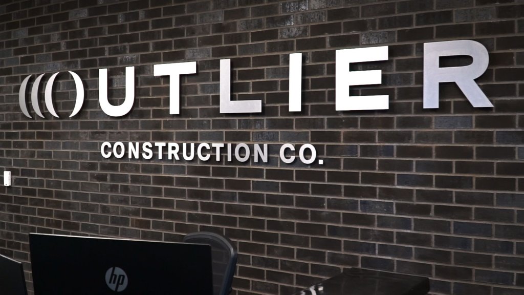 Outlier Construction sign on brick wall.