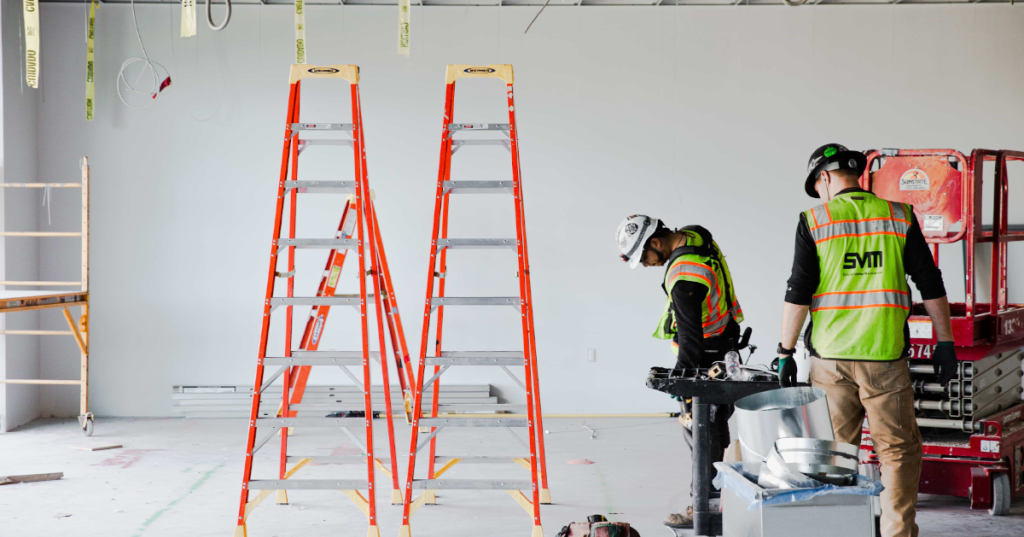 two construction workers on jobsite with ladders.