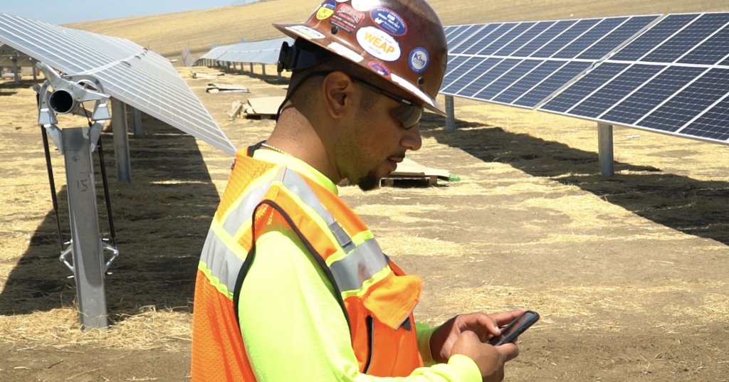 construction worker on phone next to solar panels.