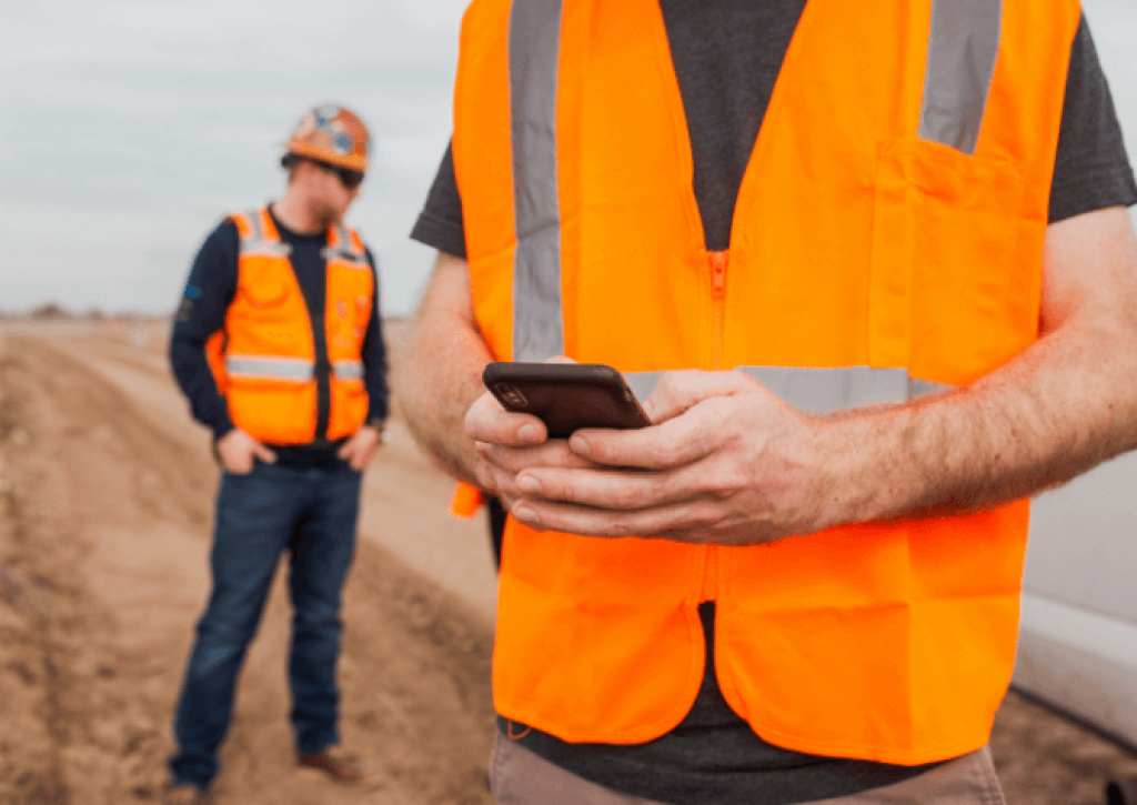 Construction worker texting material updates with mobile phone.